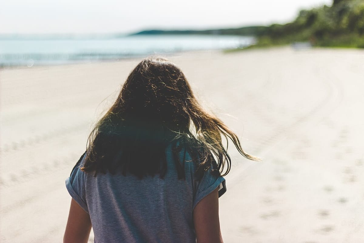 Mujer de pelo oscuro largo, de espaldas, caminando por una playa