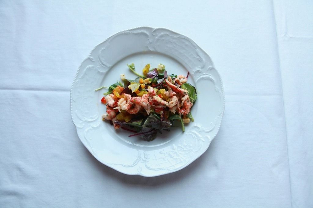 Plato blanco con una ensalada de marisco y hojas verdes sobre un mantel claro